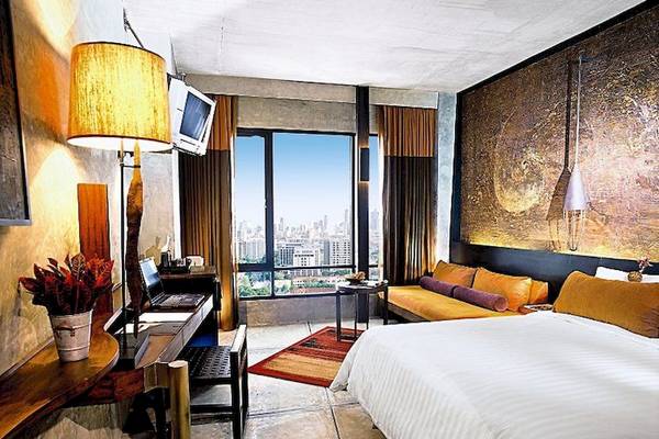 Innenansicht eines Zimmers im Siam@Siam Design Hotel Bangkok mit großem Bett, Sofa und Stadtblick.