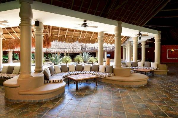 Innenbereich des Hotels Catalonia Playa Maroma mit Sitzbereichen, Tischen und Deckenventilatoren.