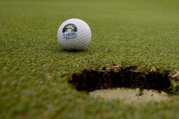 Ein Golfball mit dem Logo Caribe Golf Club liegt auf einem Golfplatz neben einem Loch.