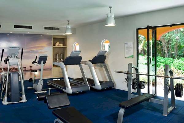 Fitnessstudio im Catalonia Playa Maroma Hotel mit Laufbändern, Kraftgeräten und Blick aufs Meer.
