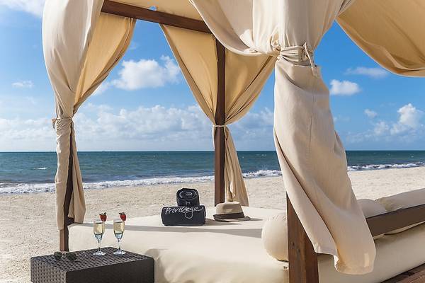 Zeltbett am Strand des Ocean Maya Royale Hotels mit zwei Gläsern Champagner und Früchten.