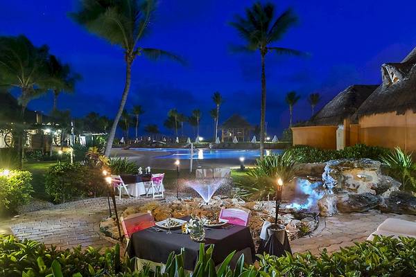Gartentisch bei Nacht im Ocean Maya Royale Hotel mit einem Wasserbrunnen und einem Swimmingpool im Hintergrund.