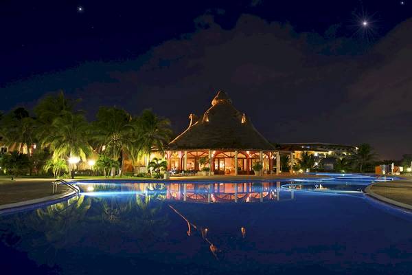 Nachtansicht des Infinity-Pools im Ocean Maya Royale Hotel mit beleuchtetem Gebäude und Sternenhimmel.