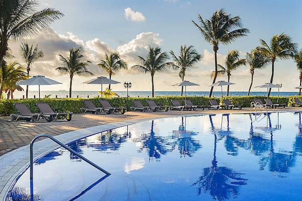 Pool-Loungebereich des Ocean Maya Royale Hotels mit Sonnenliegen und Palmen.