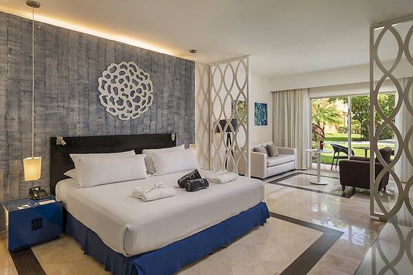 Schlafzimmer im Ocean Maya Royale Hotel mit großem Bett, weißen Kissen und blauem Boden