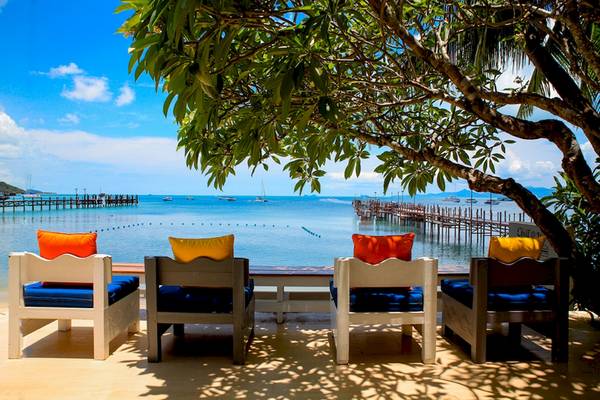 Terrasse im Punnpreeda Beach Resort mit vier Sesseln, blauen Kissen und Blick auf den Ozean und eine Pier.