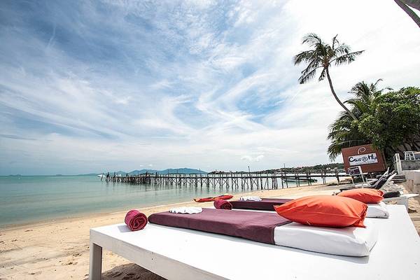 Strand des Punnpreeda Beach Resorts mit weißen Liegen und roten Kissen unter Palmen