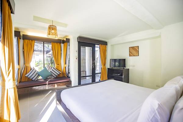 Ein Bett im Punnpreeda Beach Resort Zimmer mit gelben Vorhängen und einem Fenster mit Glastür.
