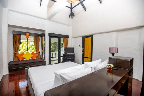 Bett im Punnpreeda Beach Resort mit weißer Bettwäsche, Holzboden und Fenstern mit Vorhängen.