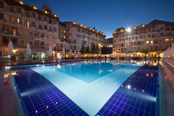 Außenpool des Side Aluna Hotels bei Nacht mit beleuchteten Gebäuden und Sonnenschirmen.