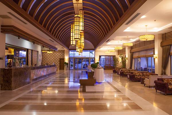 Innenansicht der Lobby des Side Aluna Hotels mit Rezeptionstresen, Sofas, und hängenden Lampen.