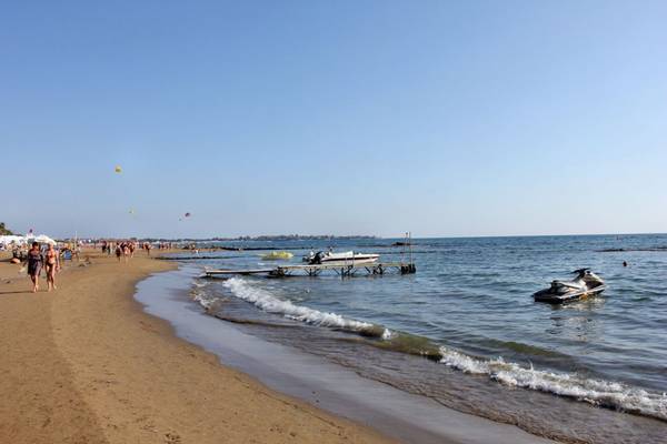 Strandszene mit gehenden Personen, Booten am Steg und Jet Ski im Wasser