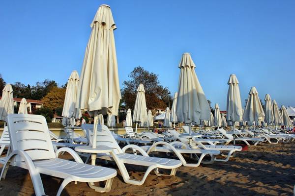 Reihen von weißen Sonnenliegen und Schirmen auf einem Strand bei blauem Himmel