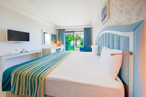 Innenansicht eines Hotelzimmers mit einem Bett, Fernseher, Schreibtisch und einem Blick auf eine Terrasse.