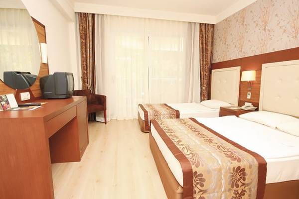 Doppelzimmer-Innenansicht im Turunc Resort mit zwei Betten, Fernseher, Spiegel und Schreibtisch.