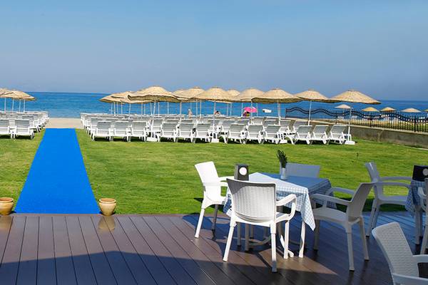 Hochzeitsfeier im Wyndham Residences Kusadasi Golf & Spa mit weißen Stühlen, blauem Teppich und Sonnenschirmen.