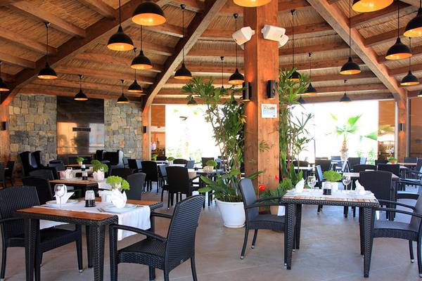 Innenbereich des Restaurants im Wyndham Residences Kusadasi Golf & Spa mit Tischen, Stühlen und Pflanzen.