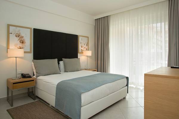 Innenansicht eines Hotelzimmers im Wyndham Residences Kusadasi Golf & Spa mit Bett, Lampen und Möbeln.