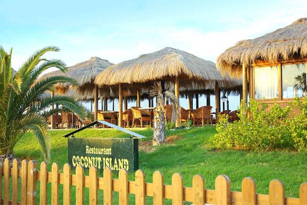Restaurant Coconut Island des El Mouradi Club Kantaoui mit strohgedeckten Sonnenschirmen und Tischen im Freien.