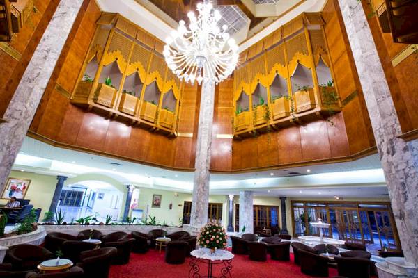 Innenansicht der Lobby im El Mouradi Palace mit einem großen Kronleuchter und vielen Sitzgelegenheiten.