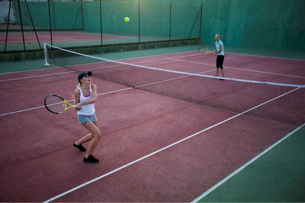 Zwei Frauen spielen Tennis auf einem roten Tennisplatz mit einer Netz und einem Tennisball in der Luft.