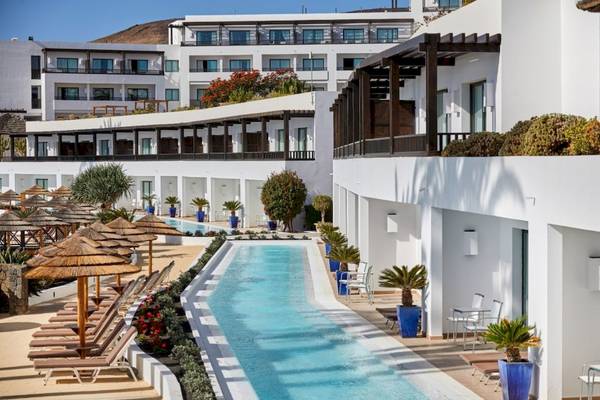 Außenpoolbereich des Secrets Lanzarote Resort & Spa mit weißen Gebäuden und Lounge-Stühlen.