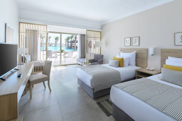 Doppelzimmer-Innenansicht im Iberotel Costa Mares mit zwei Betten, Fernseher, Schreibtisch und Poolblick.