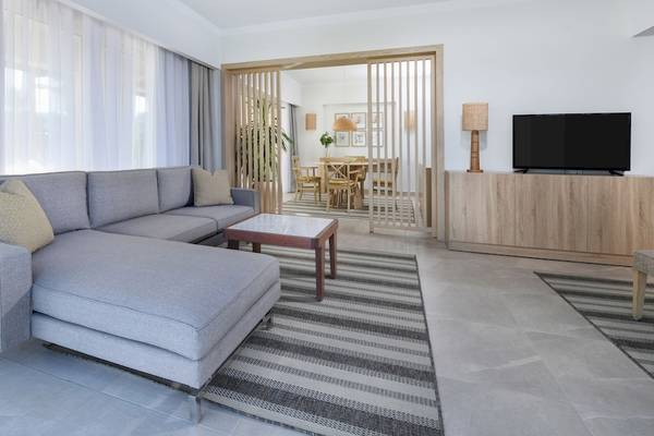 Wohnzimmer des Iberotel Costa Mares Hotels mit grauem Sofa, Couchtisch, Fernseher und Tisch mit Stühlen.
