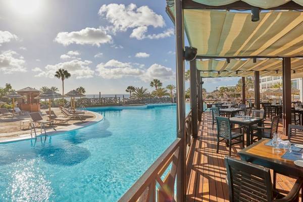 Poolterrasse des Secrets Lanzarote Resort & Spa mit Tischen und Sonnenschirmen.