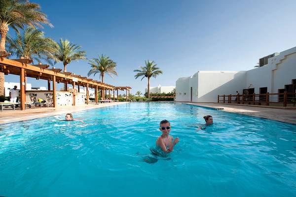 Schwimmer im Pool des Sharm Resort, umgeben von Palmen und Gebäuden.