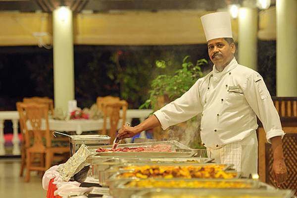 Koch in weißer Uniform bereitet Speisen auf einem Buffet im Holiday Island Resort & Spa zu.