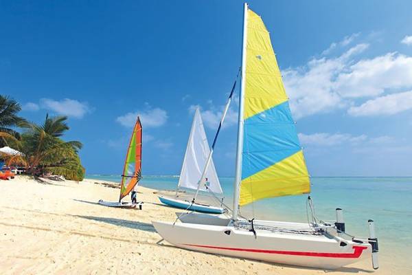 Drei Segelboote stehen auf einem weißen Sandstrand neben Palmen und klarem Wasser.