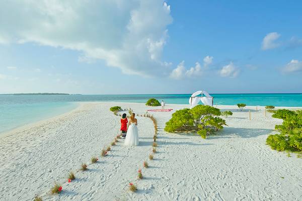 Hochzeit auf dem Strand im Holiday Island Resort & Spa mit Braut und Trauzeugen, die einen Blumenweg entlanggehen.