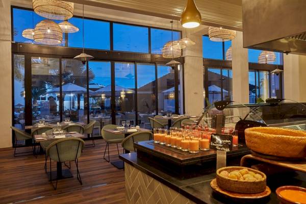 Innenansicht des Restaurants im Secrets Lanzarote Resort & Spa mit Tischen, Stühlen und Aussicht auf den Außenbereich.