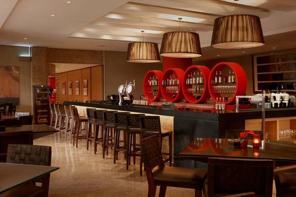 Bar im Amwaj Rotana Hotel mit roten Rundregalen und hängenden Lampen.