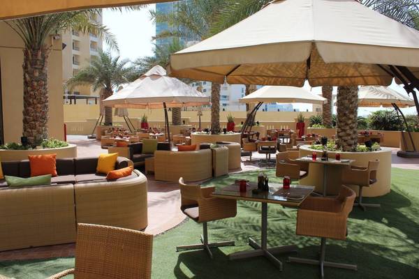 Außenterrasse des Amwaj Rotana Hotels mit Tischen, Stühlen und Sonnenschirmen.