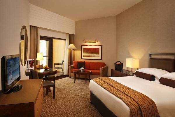 Hotelzimmer im Amwaj Rotana mit einem großen Bett, einem Sofa, einem Fernseher und einem Tisch.