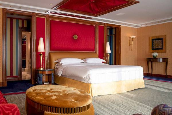 Schlafzimmer im Burj Al Arab Jumeirah Hotel mit rotem Wanddesign, goldenem Bett und zwei Nachttischen.