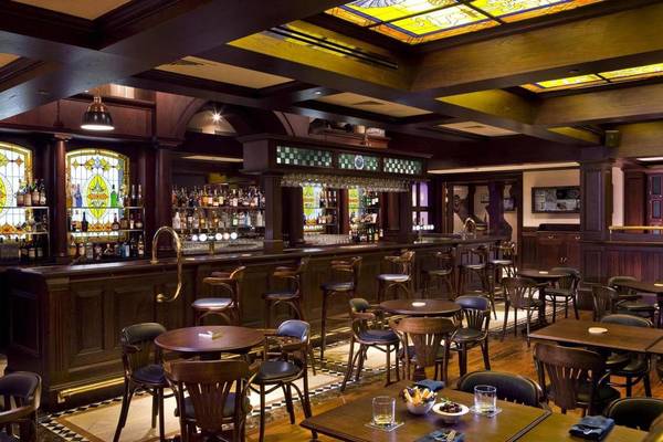 Innenansicht der Bar im Four Points by Sheraton Bur Dubai mit Holztischen, Stühlen und einem Tresen mit Glasfenstern.