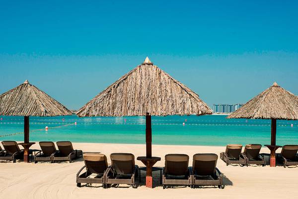 Lounge-Sessel unter Strohdächern am Strand des Le Meridien Mina Seyahi Beach Resort & Waterpark