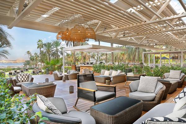 Außenterrasse des Le Meridien Mina Seyahi Beach Resort & Waterpark mit Rattanmöbeln und einer Dachkonstruktion.