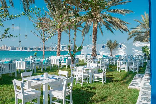 Außenbereich des Le Meridien Mina Seyahi Beach Resort & Waterpark mit weißen Tischen und Stühlen auf einer Wiese.