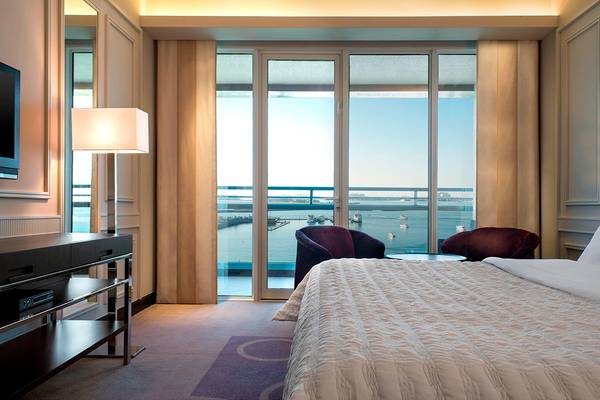 Luxuriöses Hotelzimmer im Le Meridien Mina Seyahi mit Meerblick und zwei Sesseln neben dem Bett.
