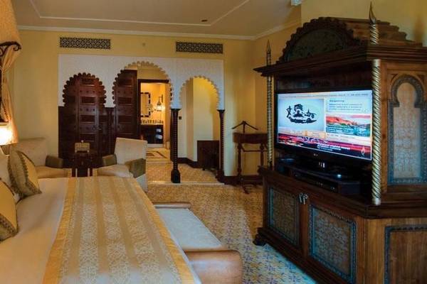 Innenansicht eines Schlafzimmers im Jumeirah Al Qasr Hotel mit einem großen Bett, Fernseher und Dekorelementen.