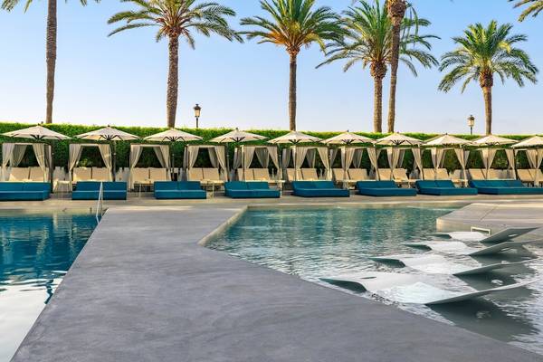 Der Poolbereich des W Ibiza mit Loungesesseln, Sonnenschirmen und Palmen im Hintergrund.