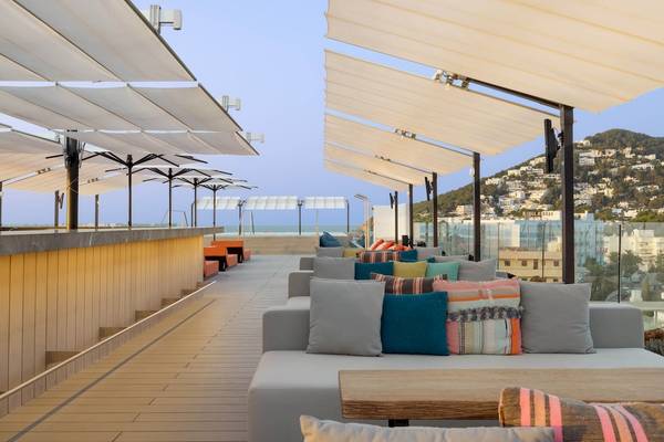 Terrasse des W Ibiza Hotels mit Sofas, Kissen und Sonnenschirmen mit Blick auf das Meer und die Stadt