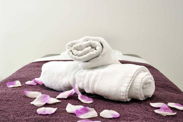 Zwei weiße Handtücher sind auf einem violetten Handtuch auf einem Bett gefaltet, mit rosa Blumenblättern verstreut.