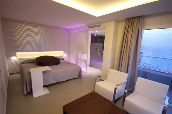 Zimmer im Sentido Garbi Ibiza mit Meerblick, mit einem Bett, zwei weißen Sesseln und einem Tisch.