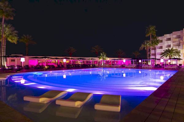 Poollandschaft des Sentido Garbi Ibiza & Spa bei Nacht, mit blauen und pinken Lichtern, Lounge-Liegen und Palmen im Hintergrund.