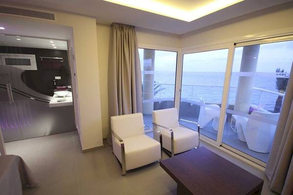 Hotelsuite mit Meerblick, zwei weißen Sesseln und einem Tisch vor großen Glastüren.